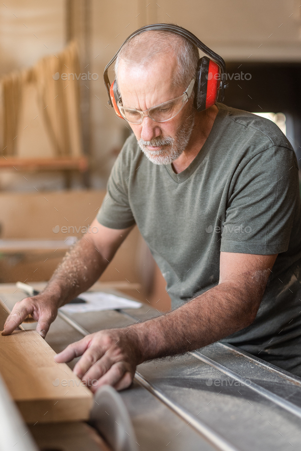Man with safety glasses cutting wood on sliding table saw Stock Photo